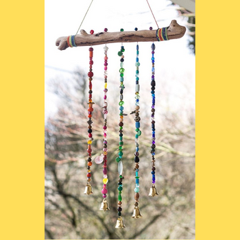 A windchime made from a stick and colourful beads hangs in front of a tree.