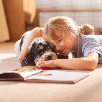 child laying beside dog while reading a story