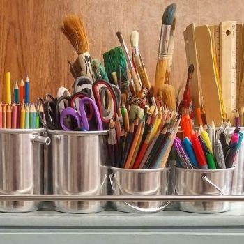 A picture of paint brushes, pencils, and other art utensils in various containers.